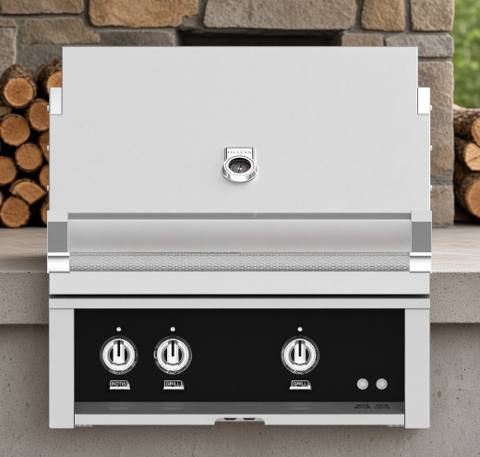 Hestan 30-inch built-in gas grill in a stone counter, stainless hood closed, black panel with three knobs.