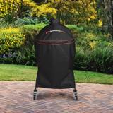 Kamado Joe Classic cover fitted over a cart grill on a brick patio, garden shrubs behind and casters below the hem