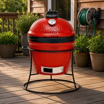 Red Kamado Joe Joe Jr in its round cast iron stand on a timber deck beside potted plants