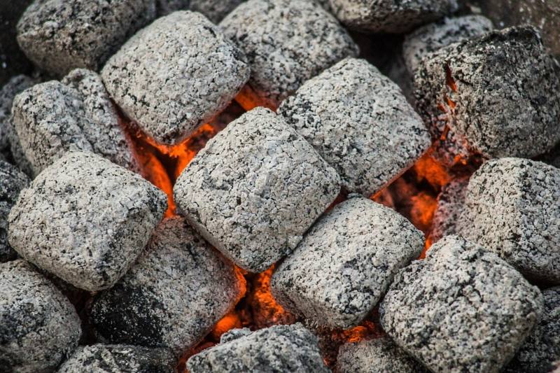 Charcoal briquettes covered in pale gray ash with an orange glow in the gaps between them