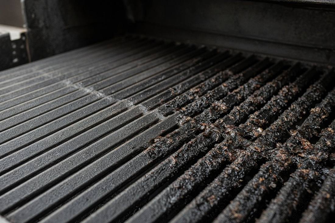 Heavy cast iron grill grates, the left half scraped clean and the right half still crusted with burnt grease