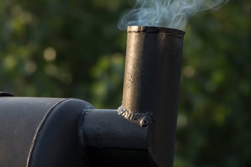 Thin, faint blue smoke rising from the chimney of a black steel smoker