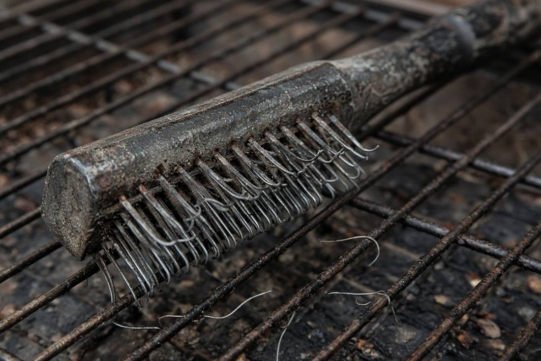 An old wire grill brush on grill grates, its bristles bent and splayed, with loose bristles lying on the grate