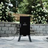 Masterbuilt analog electric smoker on its legs on a stone patio, door shut, power cord plugged in at the side