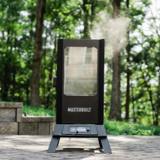 Masterbuilt 710 WiFi smoker on a stone patio among trees, smoke rising from the roof and a probe wire in the base panel