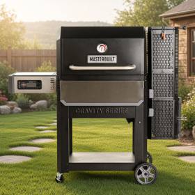 Masterbuilt Gravity Series 1050 on a lawn beside stepping stones, lid closed, charcoal hopper tower at right