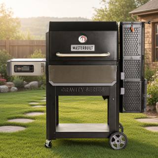 Masterbuilt Gravity Series 1050 on a lawn beside stepping stones, lid closed, charcoal hopper tower at right