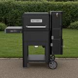 Masterbuilt Gravity Series 600 on gravel in front of a hedge, lid closed, control panel on the left shelf