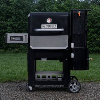 Masterbuilt Gravity Series 800 on gravel in front of a hedge, lid closed, hopper tower on the right