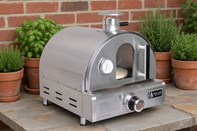 Mont Alpi stainless tabletop gas pizza oven on a stone counter beside potted herbs and a brick wall
