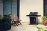 Black Rogue 425 with three knobs standing on a pale stone patio beside two wooden folding chairs