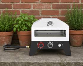 Nexgrill 12 inch gas pizza oven on a stone ledge in front of a brick wall and potted herbs