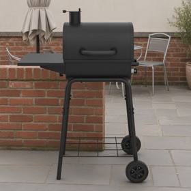 Black Nexgrill charcoal barrel grill with chimney and side shelf on gray paving beside a low brick wall