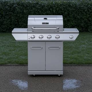 Stainless Nexgrill four-burner gas cart on wet gravel, rain-beaded lid, five knobs and two cabinet doors