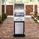 Nexgrill Deluxe 2-Burner on a brick patio with the lid raised, grates and warming rack visible, shelves out