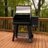 Oakford pellet grill on a wooden deck, lid open on empty cooking grid, controller lit on the hopper