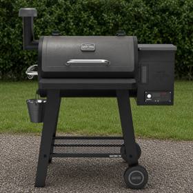 Black Nexgrill Oakford pellet barrel on a wet gravel pad by a hedge, front table down, controller lit