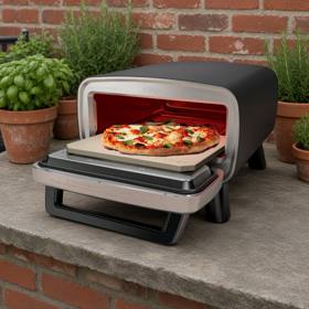 Ninja Artisan outdoor pizza oven on a stone ledge, door open with the stone pulled forward
