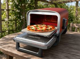 Ninja Woodfire outdoor oven on a wooden garden table, door open with a pizza on the stone