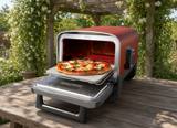 Ninja Woodfire outdoor pizza oven on a wooden garden table, door open with a pizza on the stone