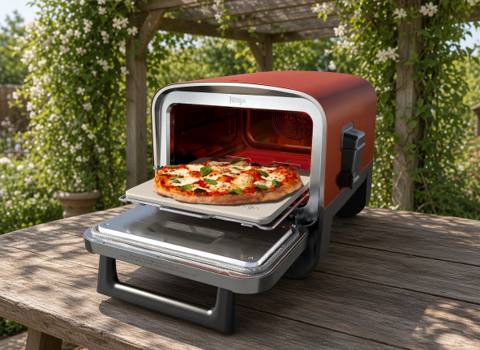 Ninja Woodfire outdoor pizza oven on a wooden garden table, door open with a pizza on the stone