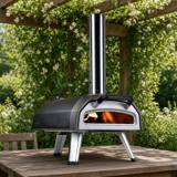 Ooni Karu 2 with its chimney and folding legs on a wooden garden table under a pergola