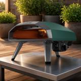 Ooni Koda 2 gas pizza oven in green on a steel outdoor table on a timber deck, burner lit