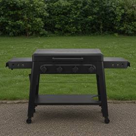 Black Traeger Irontop 4-burner griddle on wet gravel, lid closed, four control knobs and both side shelves out