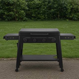 Black Traeger Irontop 4-burner griddle on wet gravel, lid closed, four control knobs and both side shelves out