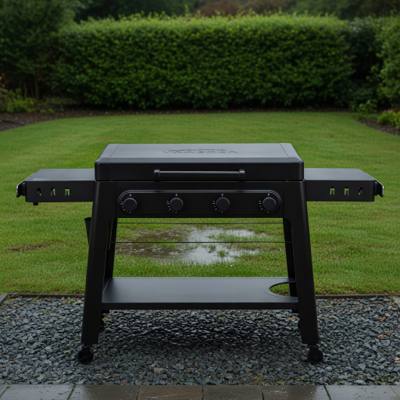 Black Traeger Irontop 4-burner griddle on wet gravel, lid closed, four control knobs and both side shelves out