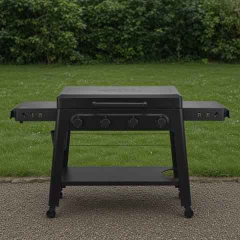 Black Traeger Irontop 4-burner griddle on wet gravel, lid closed, four control knobs and both side shelves out