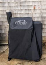 Front view of the Traeger cover on a pellet grill against shingle siding, legs and wheels showing below the hem
