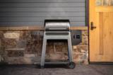 Traeger Westwood on a patio against stone and gray siding, lid closed, controller screen lit on the hopper