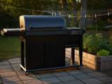 Black Traeger Woodridge Elite pellet grill on a flagstone patio at sunset, side burner left, cabinet doors closed