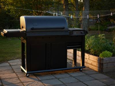 Black Traeger Woodridge Elite pellet grill on a flagstone patio at sunset, side burner left, cabinet doors closed