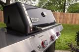 Close view of the Genesis E-315 lid and stainless control panel outdoors, Weber badge and GENESIS wordmark