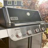 Close view of the Weber Genesis E-415 black lid, its built-in thermometer and the four control knobs