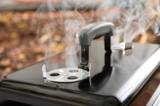 Close view of one lid damper on the Weber Go-Anywhere, its vent disc part open with smoke rising through