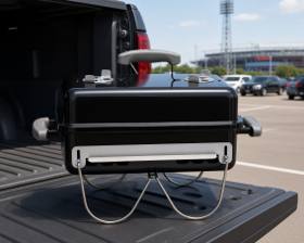 Weber Go-Anywhere charcoal grill on a pickup tailgate in a stadium car park, wire legs folded down