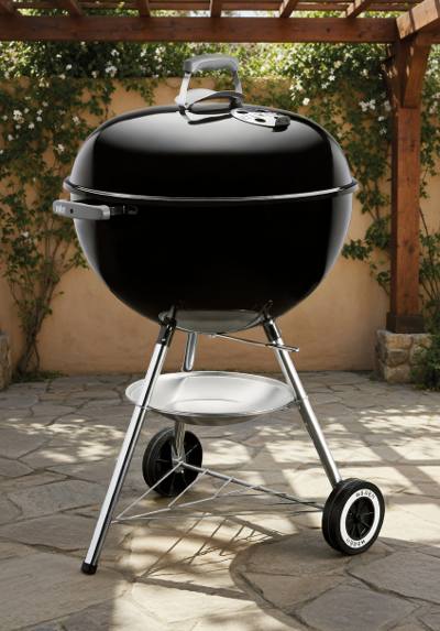 Black Weber kettle, lid closed with the lid damper showing, on chrome legs and two Weber wheels on flagstone