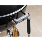 Grey nylon bowl handle on the black kettle with a grill brush and tool hanging from its two tool hooks