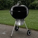 Weber Original Kettle Premium 22 inch on gravel beside a lawn, lid closed, ash catcher below the bowl