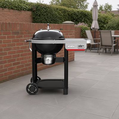 Weber Performer 22 inch charcoal grill cart on grey paving beside a brick wall, table on the right