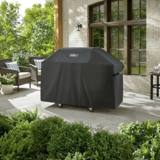 Weber Premium Grill Cover over a Genesis grill on a stone patio, wicker chairs and a brick wall behind it
