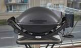 Weber Q 2400 electric grill, lid closed on a narrow balcony table, cord coiled, apartment block behind