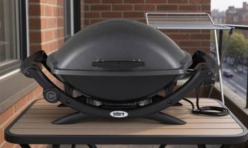 Weber Q 2400 electric grill, lid closed on a narrow balcony table, cord coiled, apartment block behind
