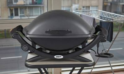 Weber Q 2400 electric grill, lid closed on a narrow balcony table, cord coiled, apartment block behind