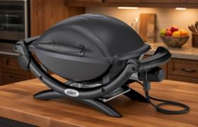 Weber Q 1400 electric grill in dark grey on a butcher block kitchen island, lid closed