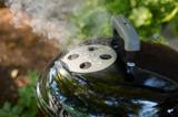 Close view of the Smokey Joe lid damper with smoke rising through it, the Tuck-N-Carry lid lock clipped alongside
