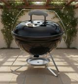 Black Weber Smokey Joe 14 kettle on a patio, lid on, chrome bail handle raised, silver ash catcher below the tripod legs